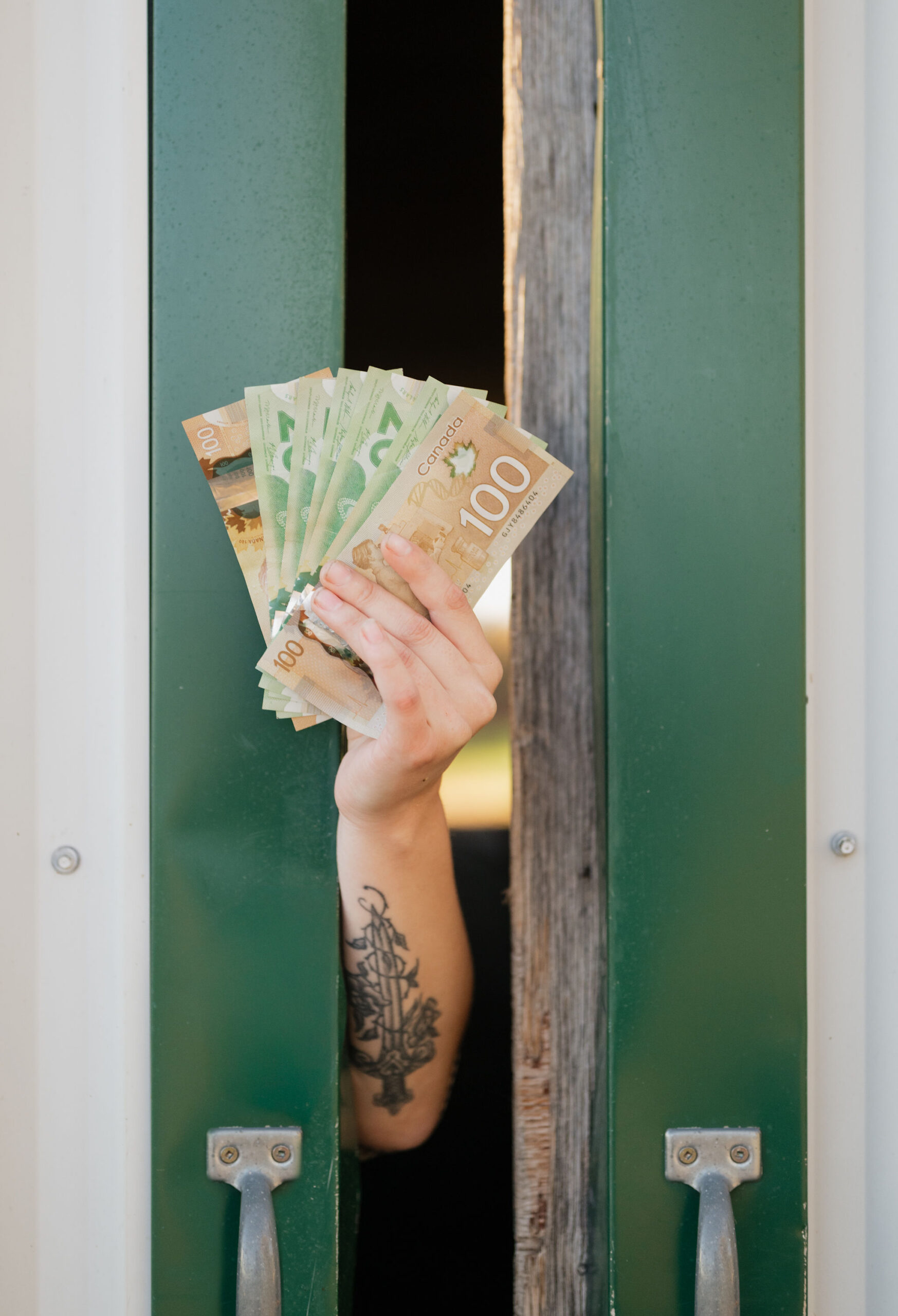 Female forearm sticking out between barn doors holding Canadian currency cash